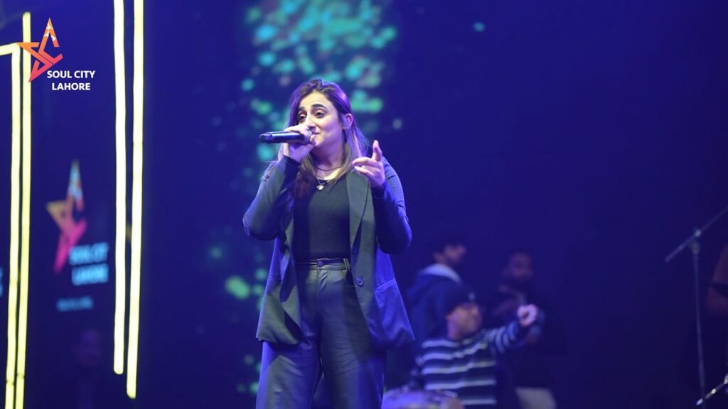 Nimra Mehra singing on stage with a microphone.